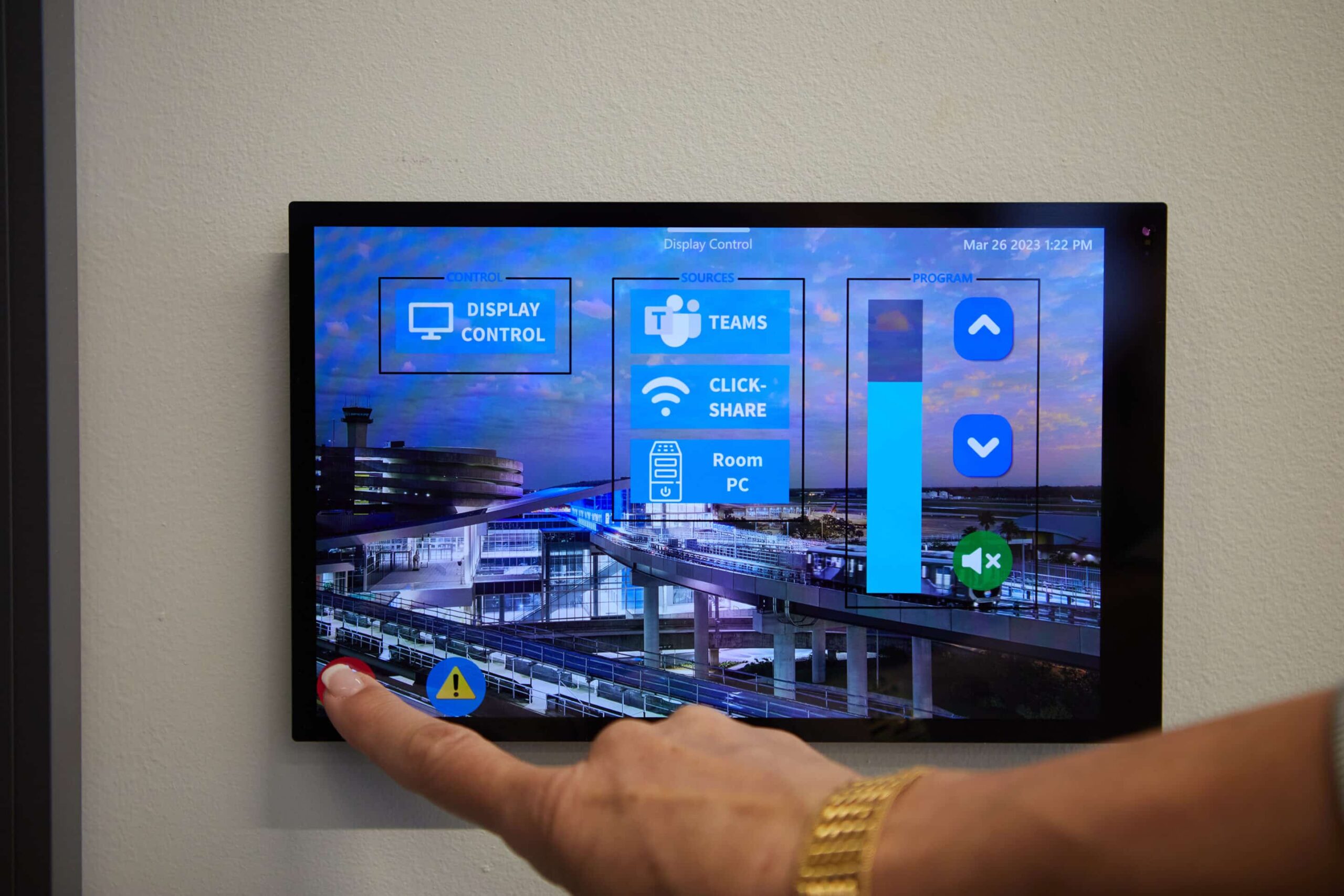 A gold-braceleted hand presses a button on a control panel with options like Display Control and CLICK-SHARE, cityscape behind.