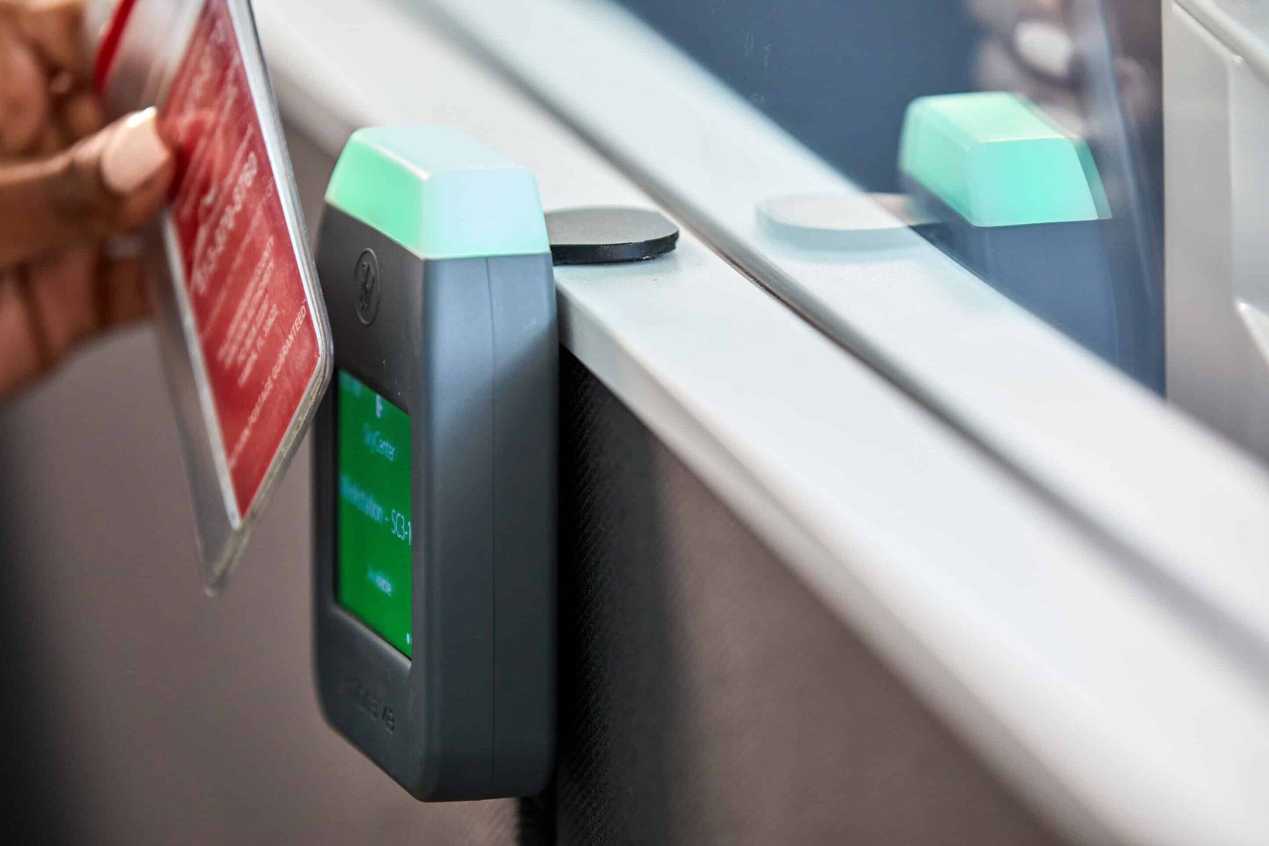 Close-up of a person with light nails holding a card near a card reader on a glass divider, green display and light visible.