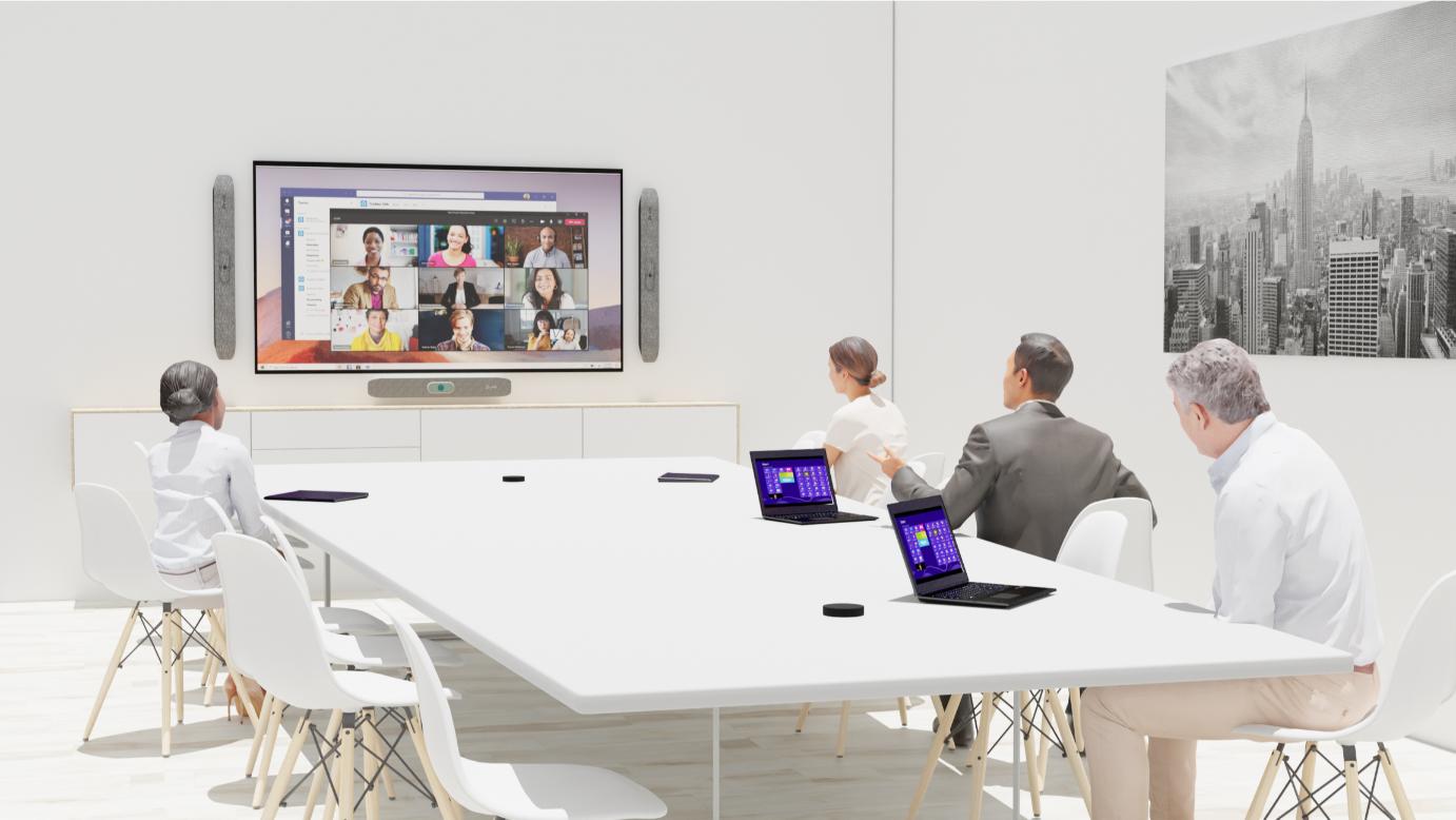 Five people at a white table with laptops in a virtual meeting; NYC skyline picture on the wall, screen shows participants.