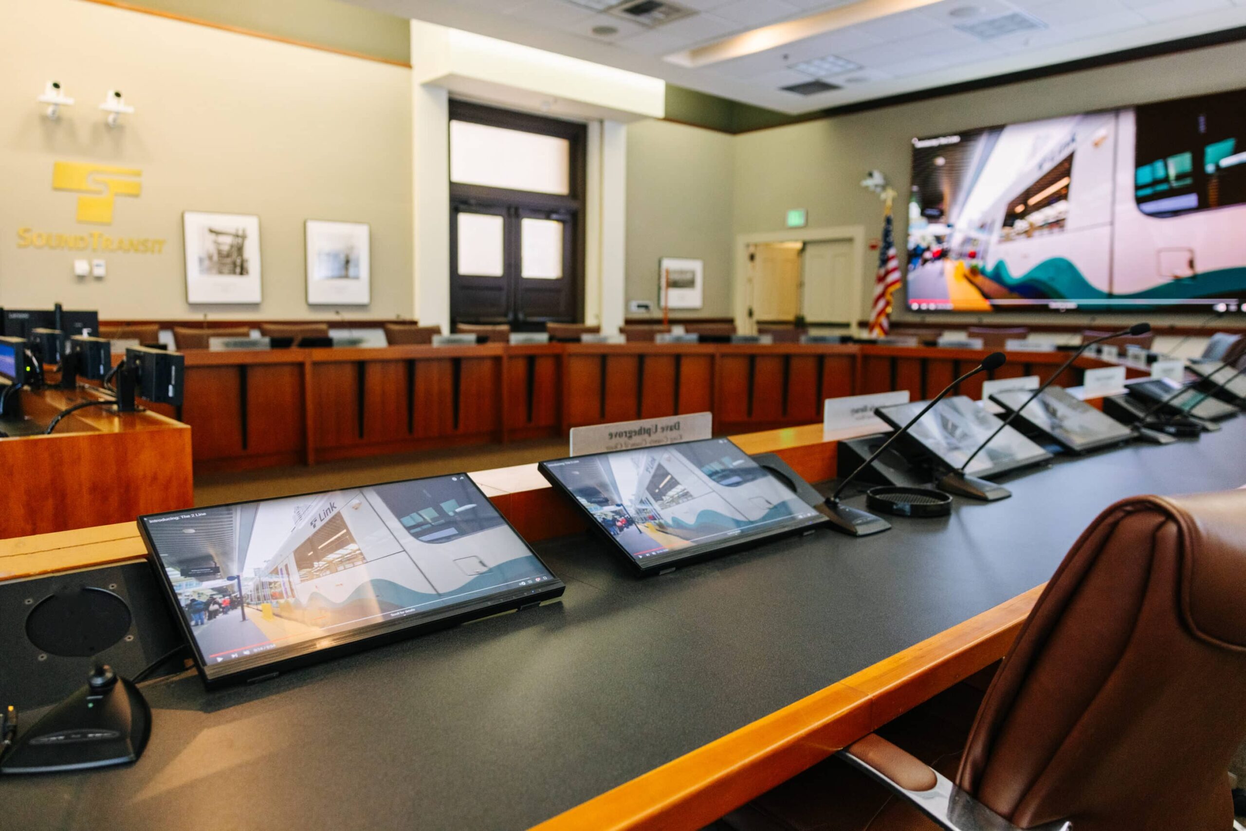 Modern conference room with large screen showing transit image, monitors on table, wood paneling, framed pictures, Sound Transit logo.