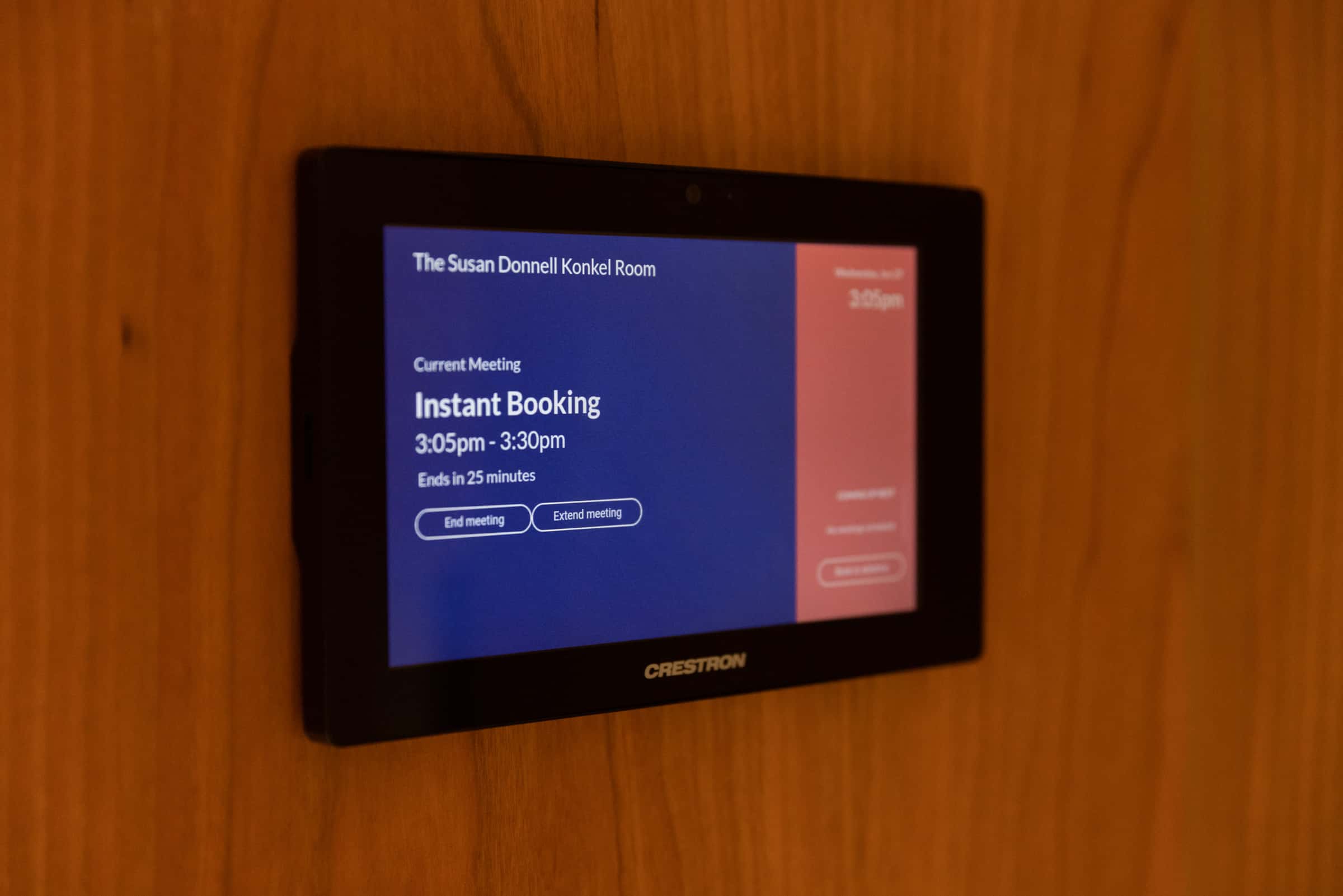 Crestron display on wooden wall: The Susan Donnell Konkel Room with ongoing meeting Instant Booking ending in 25 minutes.