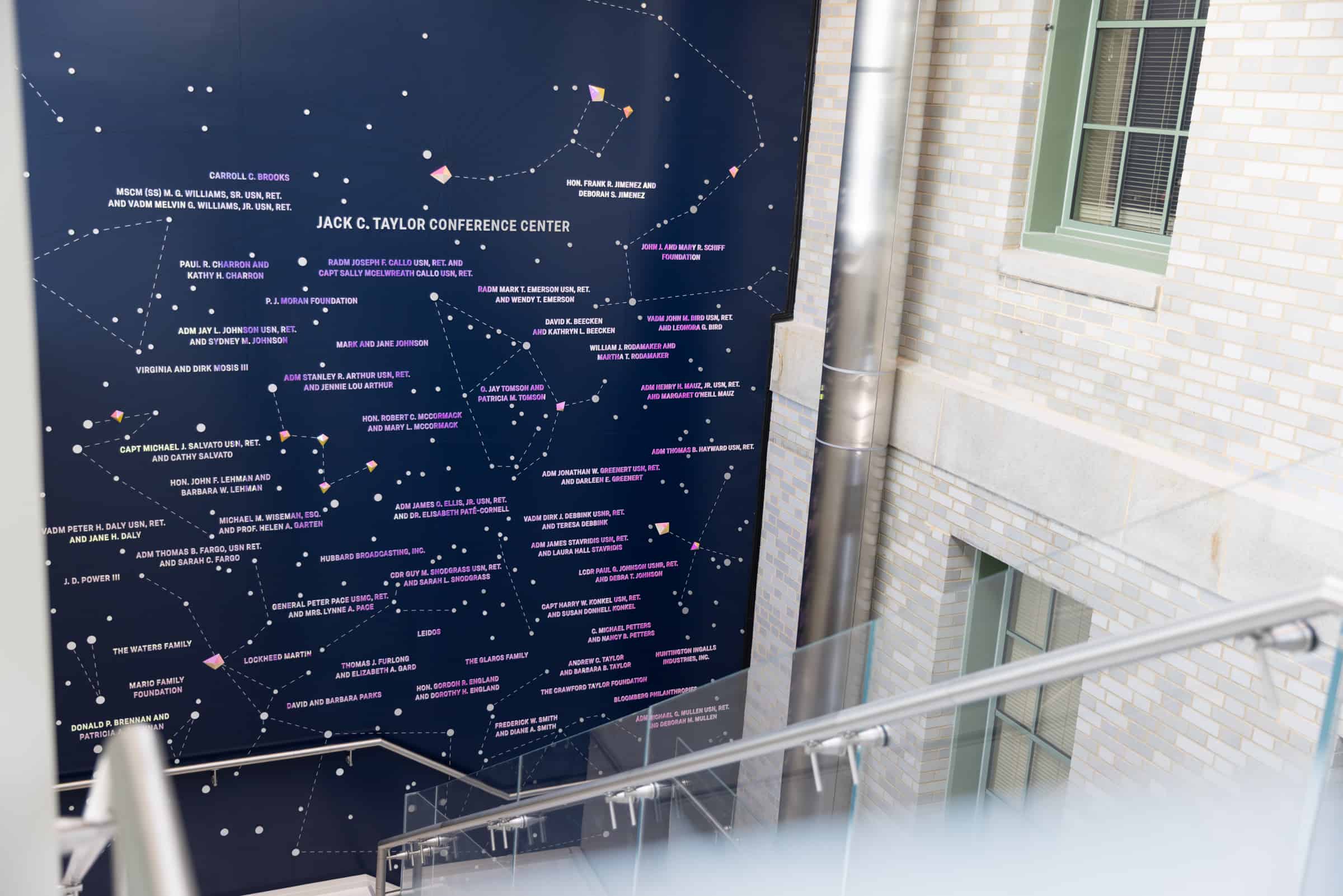 Large star map mural with labeled constellations and Jack C. Taylor Conference Center in white, beside stairwell window.